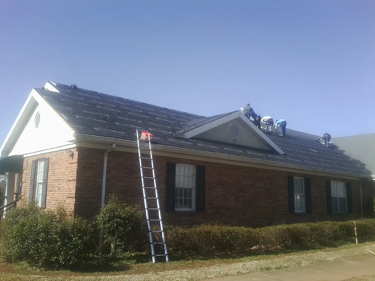 Crew tearing shingles off a brick ranch roof with a ladder set — Emergency Roof Repair work by our crew in Carlton