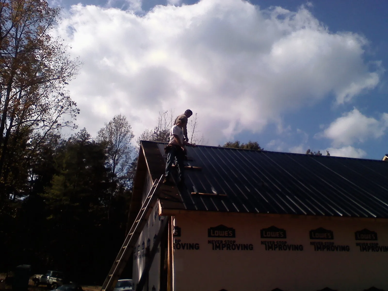 Roofer fastening dark metal panels high against a cloudy sky, from a Roof Inspection job in Carlton