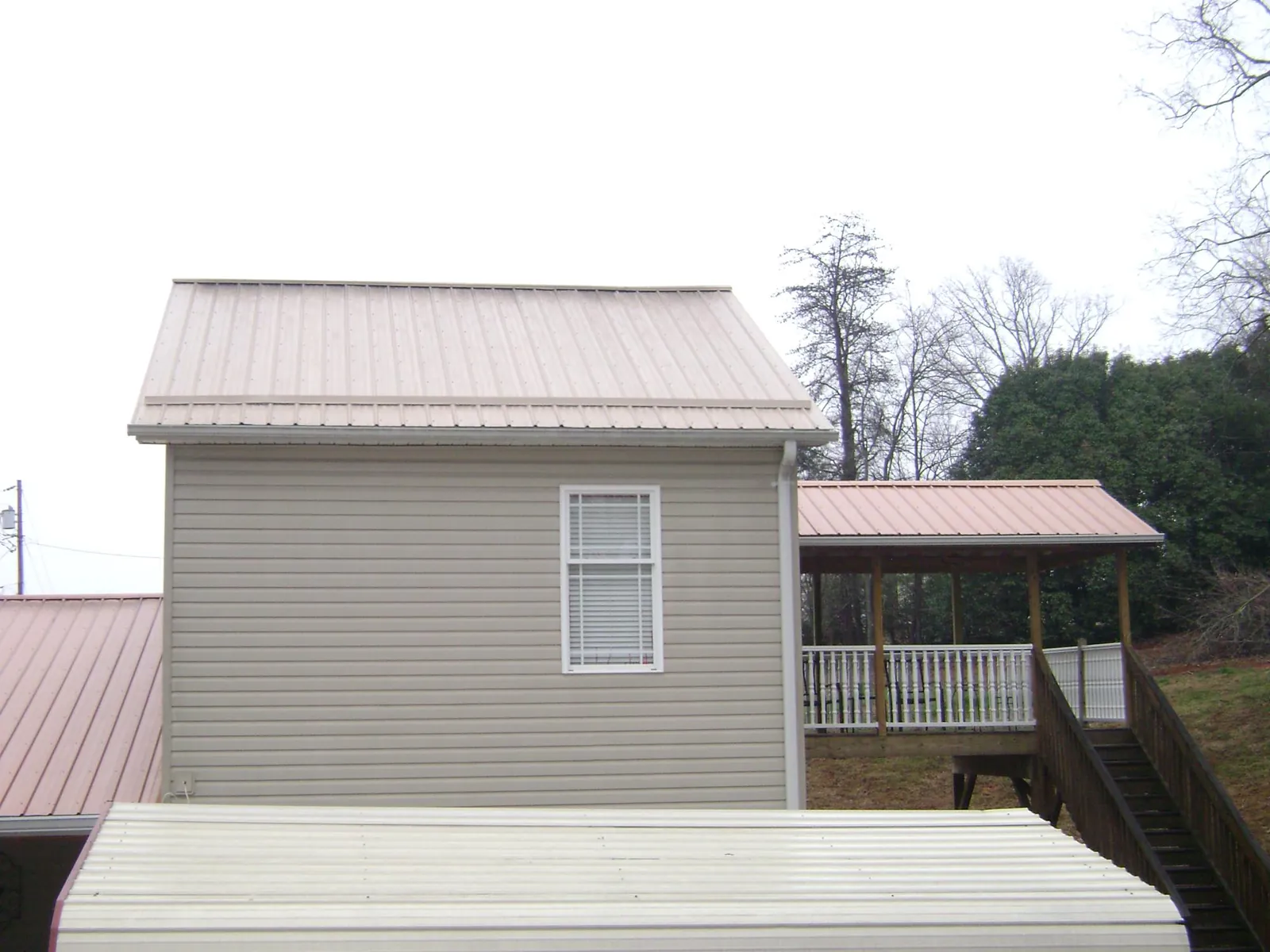 Tan metal roofs on a two story addition and attached porch, from a Roof Replacement job in Carlton
